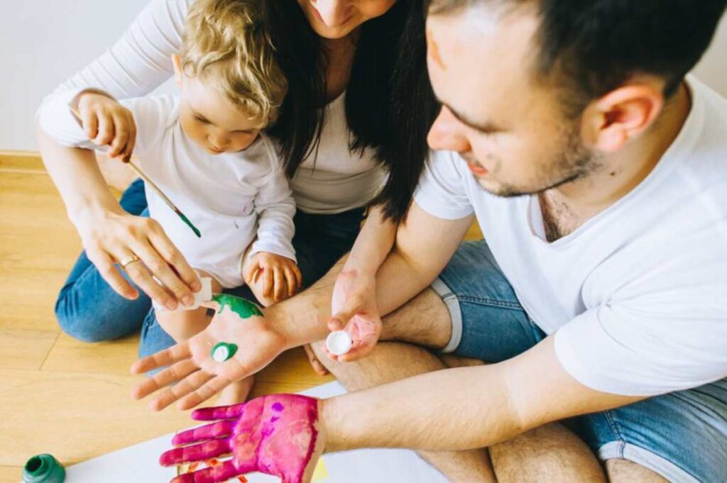 A family engages in fun arts and crafts, with colorful paint on hands and a child painting their foot.