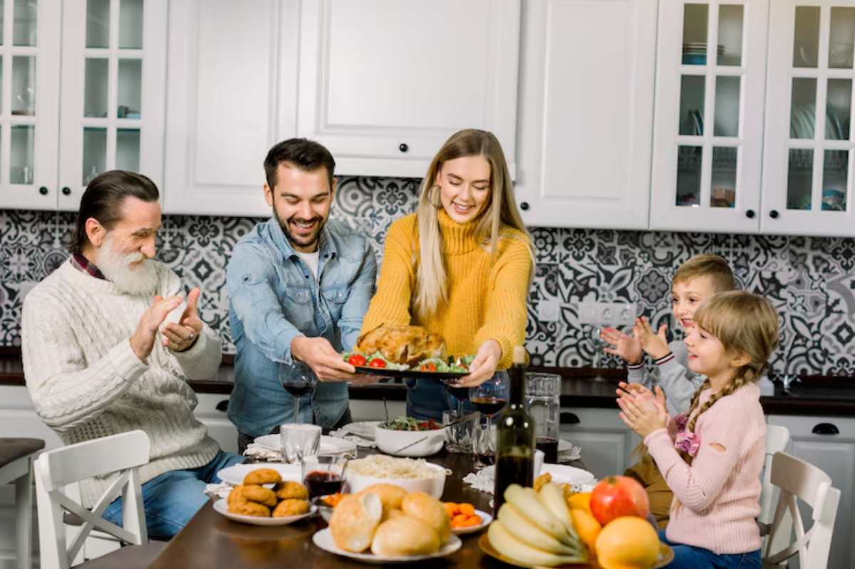 A family gathers around a table filled with food, as a woman presents a festive dish, creating a warm and celebratory atmosphere.