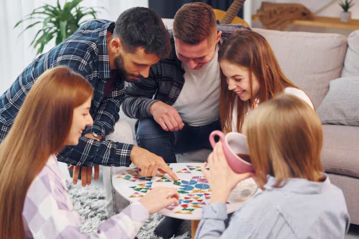 A group of friends gathered around a board game on a coffee table, engaged in conversation and teamwork.