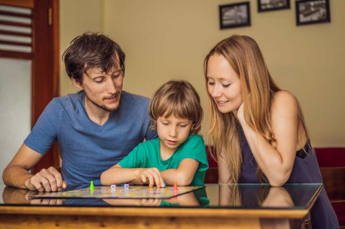 A family plays a board game together at a wooden table, showing engagement and enjoyment in a cozy, well-lit room.