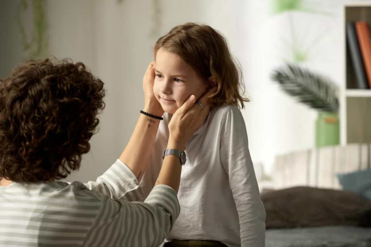 A person gently holds the shoulders of a child while talking, both in a cozy, softly lit room .