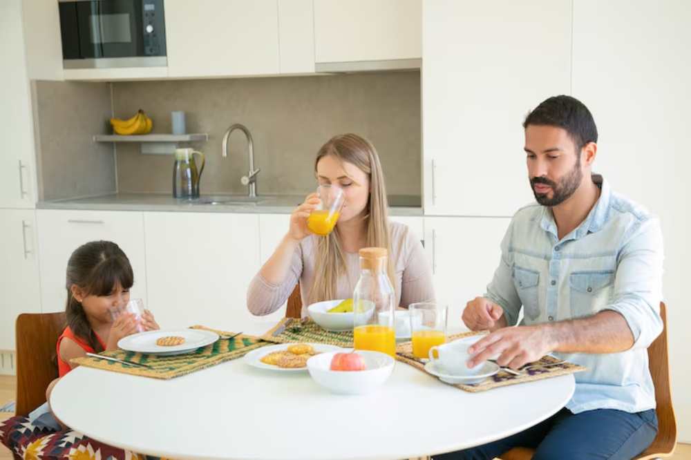 A family enjoying breakfast at a modern kitchen table, featuring fruit juice, pastries, and a warm atmosphere.