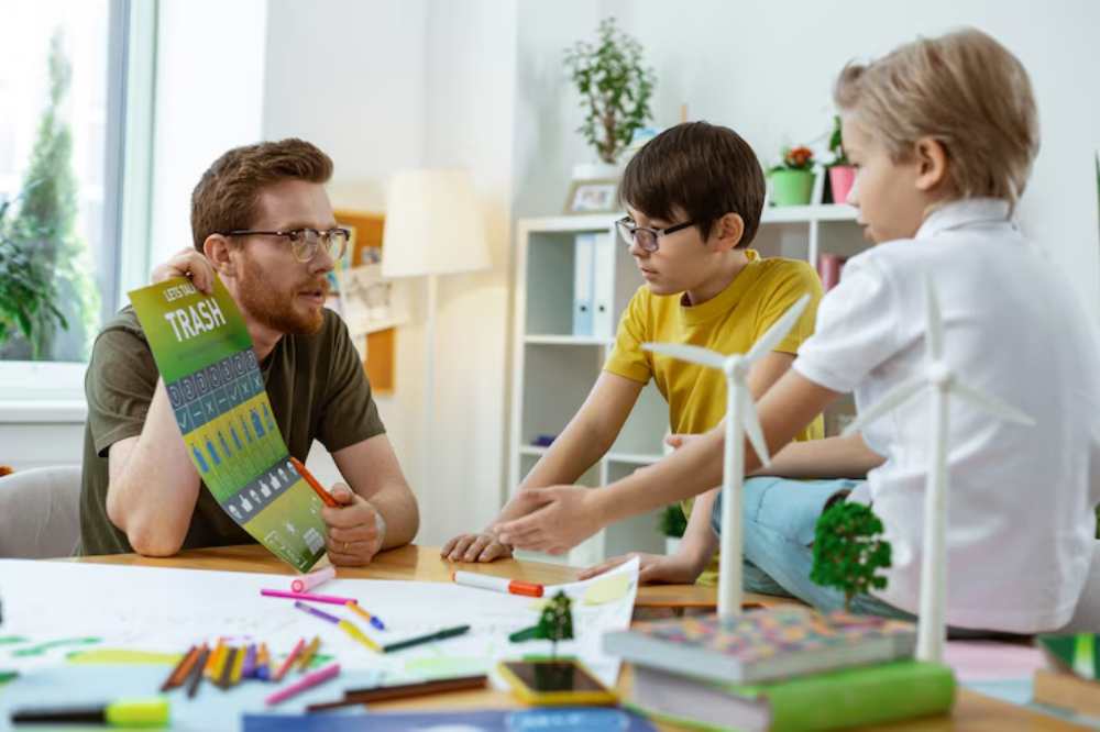 A group of children engages in a creative project at a table, surrounded by sketches, colored markers, and miniature trees and wind turbines.