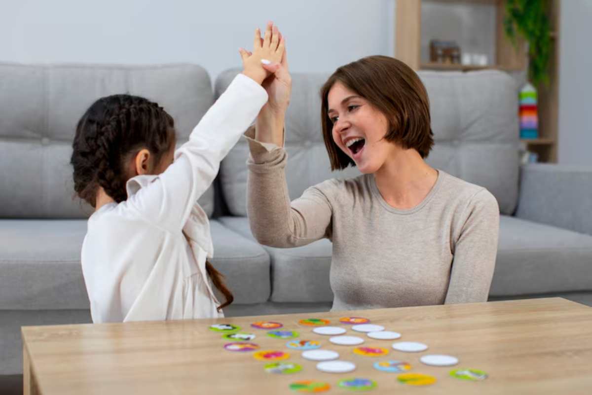 A child and an adult play a game, raising their hands in victory, with colorful game pieces scattered on the table between them.