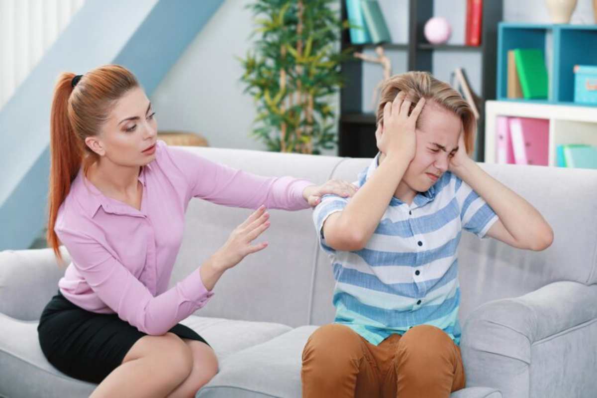A woman in a pink blouse gently reaches out to comfort a distressed boy sitting on a couch, showcasing a supportive interaction.