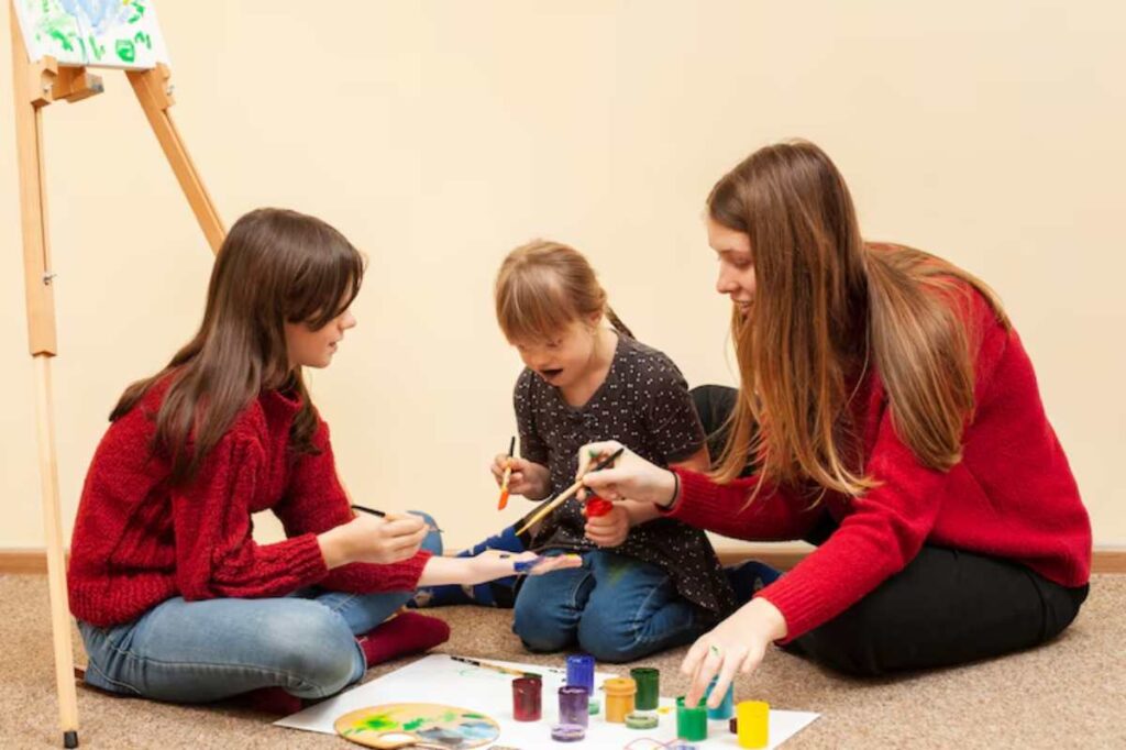 Three children are engaged in a creative painting activity on the floor, surrounded by colorful paint pots and art supplies.