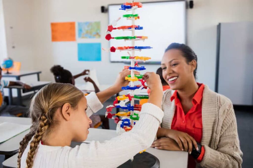A child assembling a colorful model with plastic pieces in a classroom, while an adult observes attentively in the background.