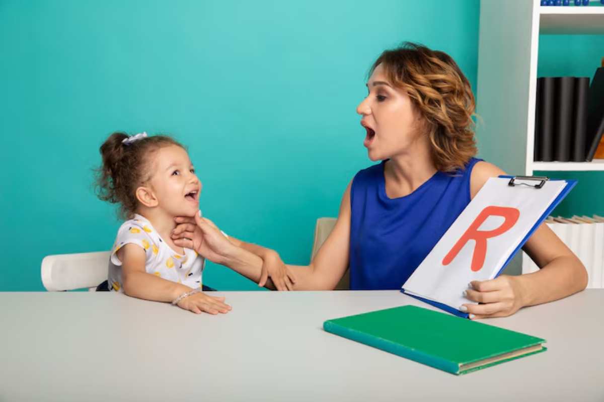 A woman in a blue top holds a clipboard with the letter 'R,' engaging with a young girl at a table against a teal background.