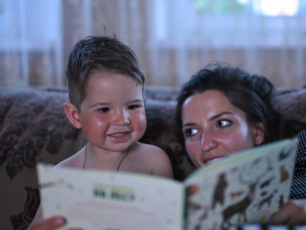 A child and an adult closely reading a book together on a couch, showcasing a cozy indoor atmosphere.