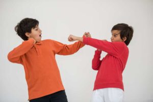 Two children playfully engage in a mock fight, one wearing an orange shirt and the other in red, both showing dynamic movement.