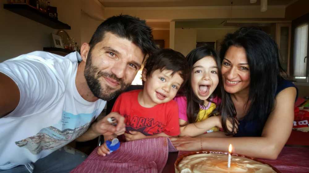 A family gathered around a table with a cake and a lit candle, celebrating an occasion in a cozy indoor setting.