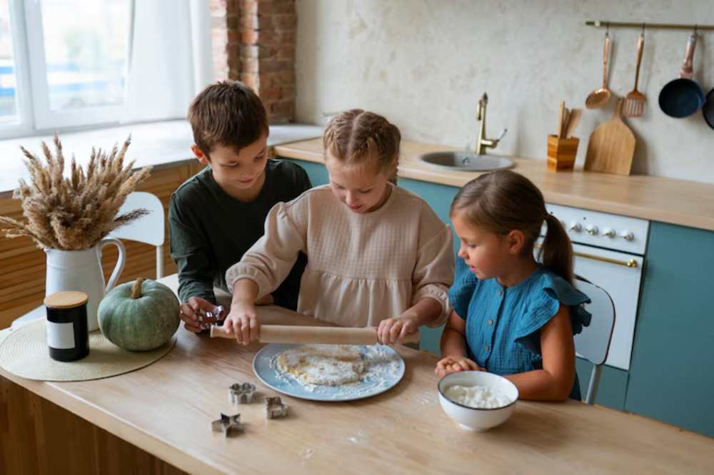 Three children work together in a cozy kitchen, rolling dough on a plate while surrounded by baking tools and ingredients.