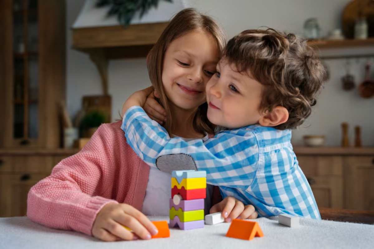 A child in a blue checkered shirt embraces a girl in a pink cardigan at a table with colorful building blocks.