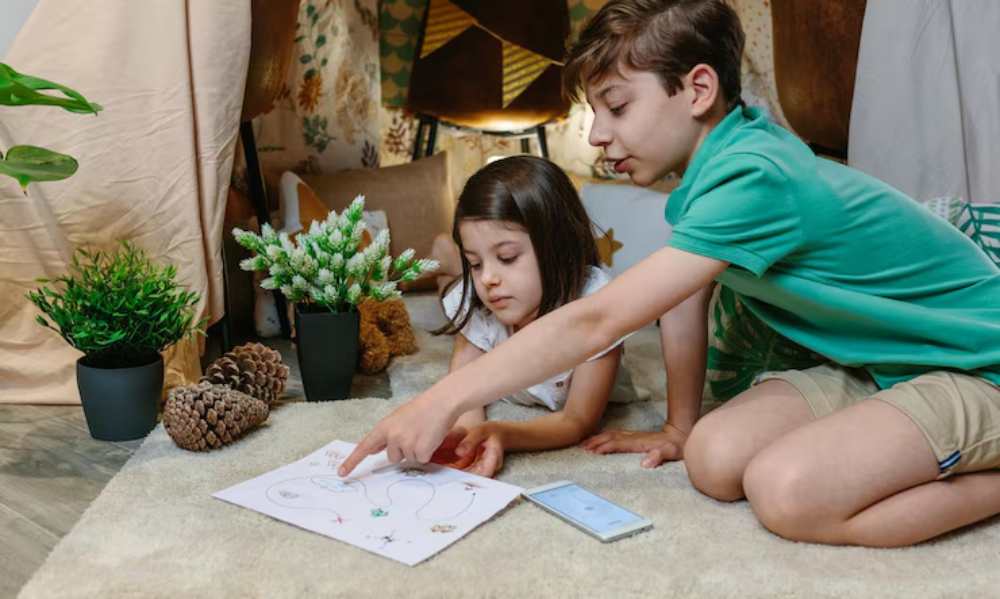 Two children are engaged in a creative activity on a soft rug, surrounded by plants and cozy decor. They're examining drawings and a phone.