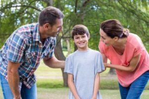 A man and woman converse warmly with a teenager in a park, surrounded by greenery, creating a nurturing and supportive atmosphere.